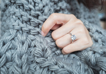 Close up of an elegant engagement diamond ring on woman finger with dark gray sweater winter clothe. love and wedding concept. love and wedding concept. Soft and selective focus. - obrazy, fototapety, plakaty