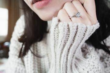 Close up of an elegant engagement diamond ring on woman finger with beige sweater winter clothe....