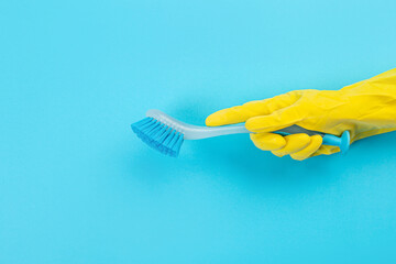 A hand in a yellow glove holds a plastic cleaning brush on a blue background. Banner with copy space. Chemical cleaners, household chemicals, brushes and collage supplies. Cleaning concept.