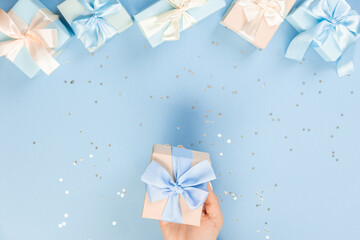 Woman hands holding gift or gift box decorated with confetti on blue pastel table top view. Flat composition for birthday or wedding.