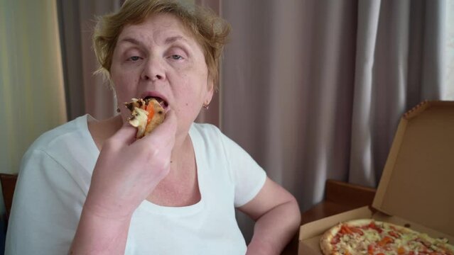 senior fat woman eating delicious slice of pizza at home with cheese, tomato and chicken, closeup