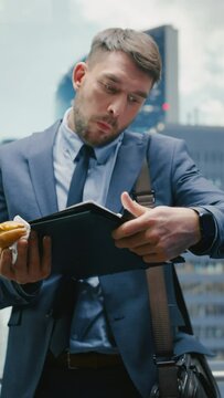 Vertical Screen: Business Manager is Late for Work, Riding Glass Elevator in Modern Office Building. Handsome Man Eating a Tasty Take Away Hamburger in a Hurry on Way to Corporate Meeting in a Lift.