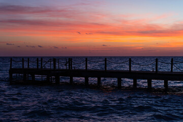 Fototapeta na wymiar Rope bridge silhouette at sunset. Beautiful seascape, bright orange sky and sea