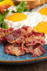 Closeup on fried bacon in a plate with eggs and salad breakfast