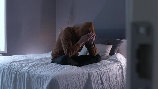 Sad man alone, sitting on bed crying