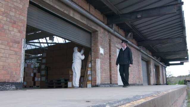 A security guard is checking a pharmaceutical lab warehouse building as scientists and technicians close the shutter doors.