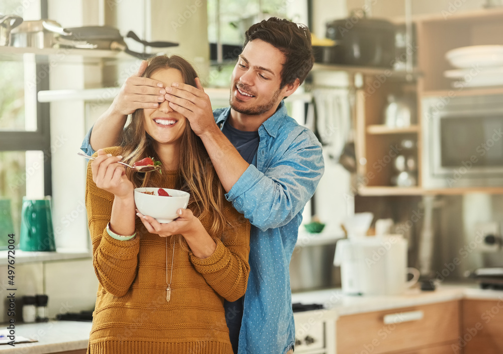 Canvas Prints Guess who. Shot of an affectionate young man covering his girlfriends eyes while she eats breakfast in their kitchen.