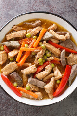 Filipino food Igado is a popular Ilocano dish made from pork tenderloin and innards with vegetables closeup in the plate on the table. Vertical top view from above