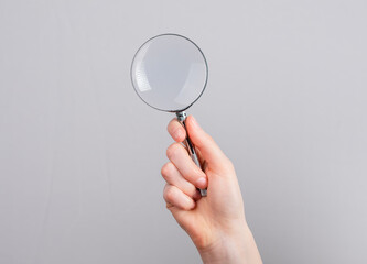 Obraz na płótnie Canvas Hand holding magnifying glass. Information search, key words finding, data analysis and verification concept. Lupe on grey background. High quality photo