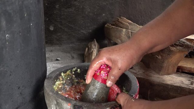 A woman preparing red Mexican salsa on a molcajete.