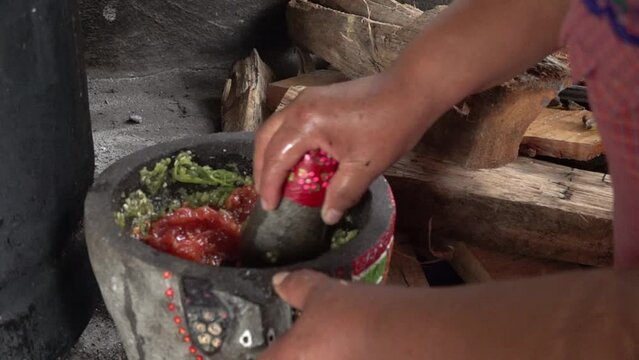 A Mexican woman crushing tomatoes on a molcajete.
