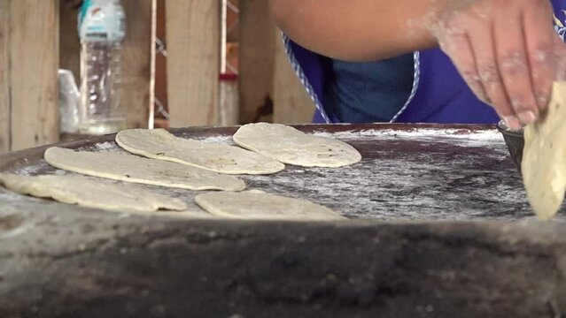 A woman flipping tortillas on a comal.