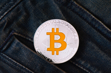 A silver Bitcoin cryptocurrency coin protrudes from the pocket of blue frayed jeans. Virtual money...