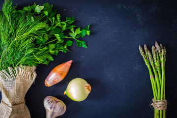 Fototapeta na wymiar Bunch of parsley, dill, coriander, onion, garlic and asparagus on black table