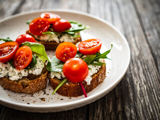 Tasty sandwiches - toasted bread with cream cheese, cherry tomatoes and green leaves on wooden table
