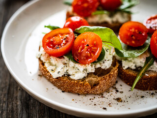 Tasty sandwiches - toasted bread with cream cheese, cherry tomatoes and green leaves on wooden table
