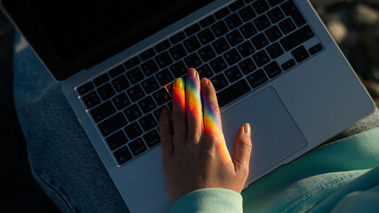 A woman is typing on a laptop. Rainbow light from a prism. 