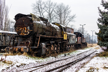 Plakat Old, rusty, demolished steam locomotive standing on the side track of the train station. Picture taken in cloudy winter day.