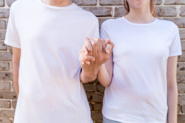 Couple wearing mockup white t-shirts on brick wall background holding hands. Template fashion copy space