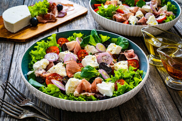 Tasty salad - prosciutto di Parma, feta cheese and fresh, green vegetables on wooden table