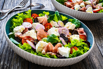 Tasty salad - prosciutto di Parma, feta cheese and fresh, green vegetables on wooden table