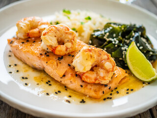 Fried salmon steak with prawns, white rice and spinach on wooden table
