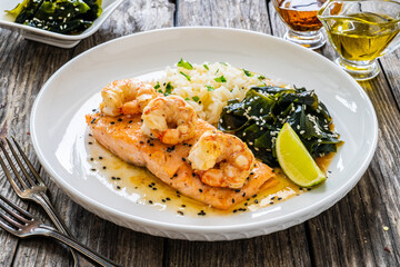 Fried salmon steak with prawns, white rice and spinach on wooden table
