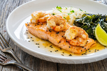 Fried salmon steak with prawns, white rice and spinach on wooden table
