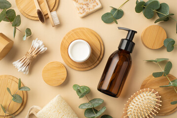 Eco cosmetics concept. Top view photo of glass dispenser bottle cream jar soap hair brush eucalyptus cotton buds toothbrushes and wooden stands on isolated beige background