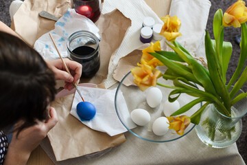 An overhead view of a table where a woman prepares for Easter by dyeing boiled eggs with a dye solution and drying them on a napkin.