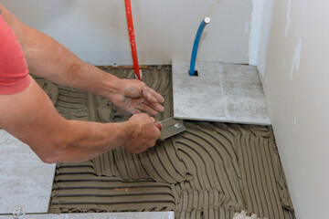 Man placing ceramic floor tile in position over adhesive in new home
