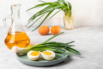 Naklejka na ściany i meble Fresh green onions, boiled eggs and vegetable oil on a light background. Simple and healthy breakfast. Copy space