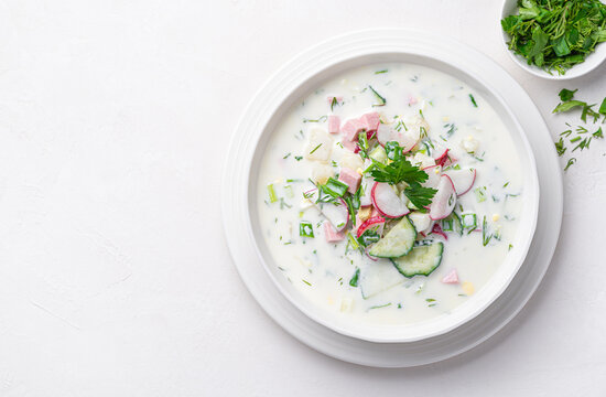 Summer, cold okroshka soup with vegetables, sausage, herbs and kefir on a white background.