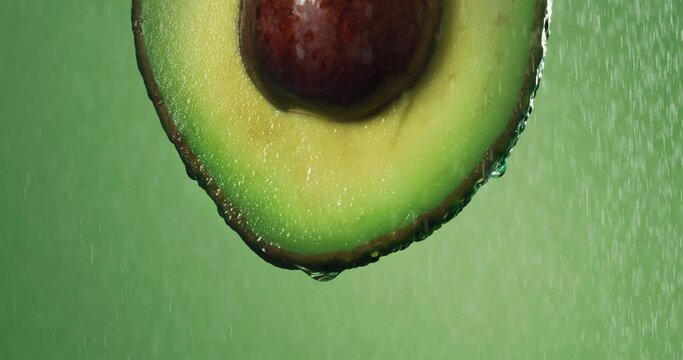 Cinematic macro shot of half raw fresh organic tropical green avocado fruit with falling water drops isolated on green background.