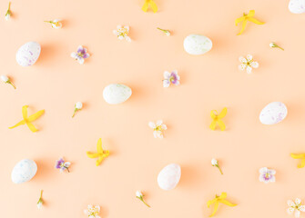 Flowers and Easter eggs arranged on a peach colored background. Minimal holiday composition pattern flat lay.