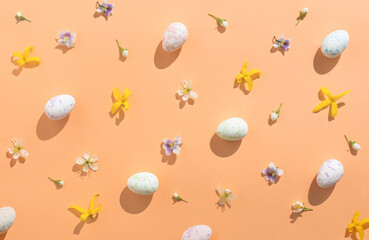 Flowers and Easter eggs arranged on a peach colored background. Minimal holiday composition pattern flat lay.