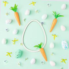 Easter eggs,carrots and flowers arranged on a pastel green background with an egg shaped copy space. Holiday flat lay minimal composition.