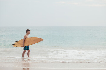 Fototapeta na wymiar A handsome teenage boy with a surfboard going into the ocean on a sandy beach on the surf line of Sri Lanka.