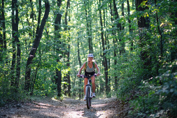 Obraz premium Front view of active senior woman biker cycling outdoors in forest.