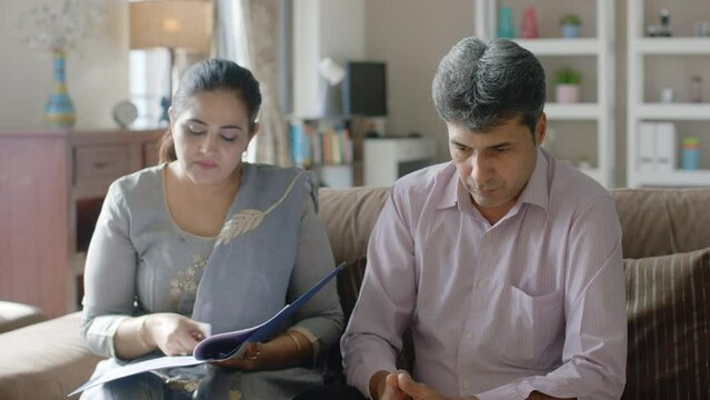 Upset Indian Man and Woman or Husband wife sitting together filing a divorce or signing documents or papers with mutual consent with Lawyers help in the interior home. Separation, break up concept