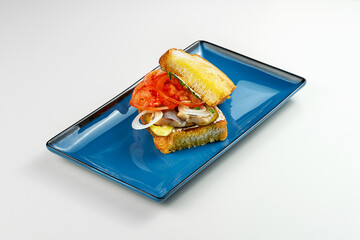 Toast with herring and tomatoes in a blue plate. Gray background. Close-up