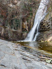 Mountain landscape. The waterfall flows into a mountain river. Around the rock. In the foreground is a huge rock mass. Beautiful waterfall. vertically. Travel. copy space. No people.