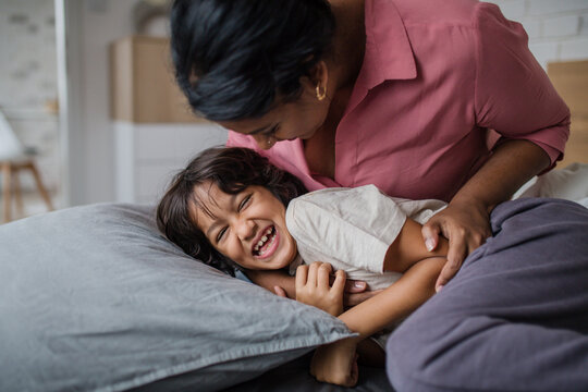Happy mother tickling her little son when waking him up in morning.