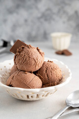 Three brown chocolate ice cream balls, scoops in white bowl on gray background