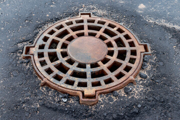 Cast-iron manhole of the storm sewer system on the road in front of the asphalt pavement.