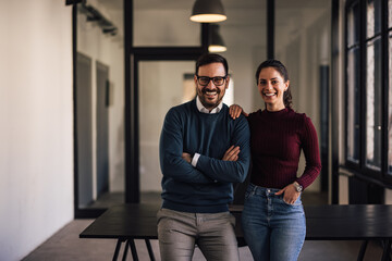 Portrait of two colleagues, standing next to each other, smiling at the camera.