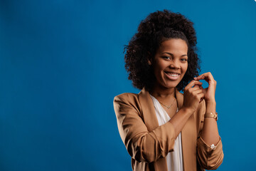 Laughing african-american woman, holding her strand of hair with two hands, blue background.