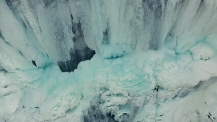 Aerial close up shot of top view of frozen crystal iced waterfall icicles in snowy mountains in winter. - Powered by Adobe
