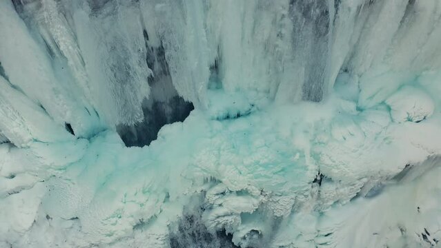 Aerial close up shot of top view of frozen crystal iced waterfall icicles in snowy mountains in winter.