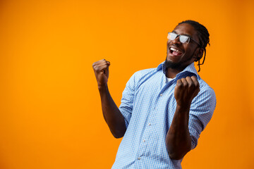 Portrait of overjoyed black man celebrating success with clenched fists against yellow background